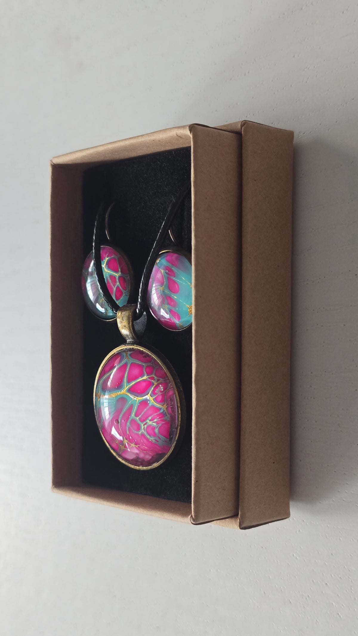 Cabochon-Schmuckset mit rundem Anhänger und zwei Ohrringen in kräftigem Pink und Türkis mit feinen goldenen Zellstrukturen und schwarzem Textilband.
