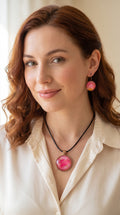 Frau trägt Cabochon-Schmuckset mit Anhänger und Ohrringen in Pink- und Rosatönen mit goldenen, fliessenden Linien und schwarzem Textilband in einer Schachtel.