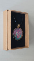 Runder Cabochon-Anhänger an schwarzem Band mit organischem, dunkel umrandetem Muster in Pink, Rosa, Türkis und warm schimmernden Nuancen.