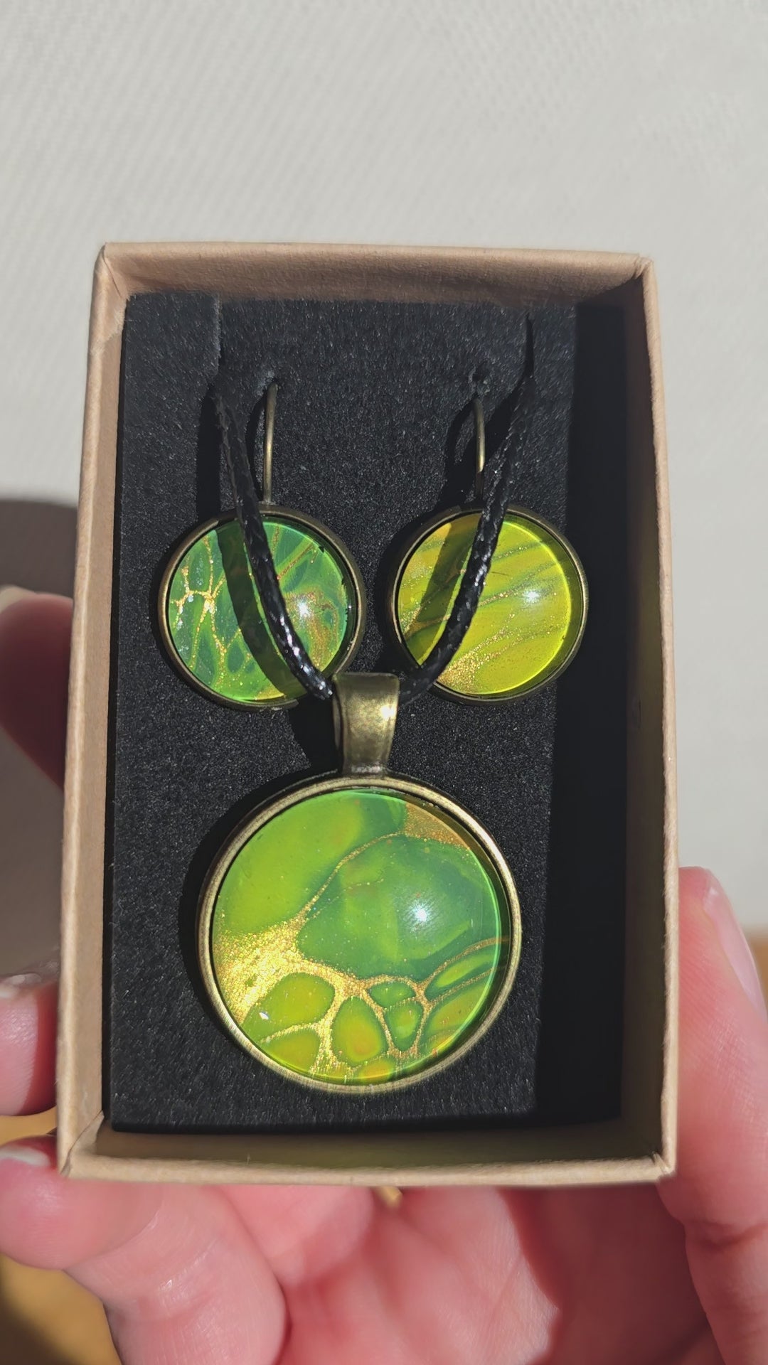 Rundes Cabochon Schmuckset mit grossem Kettenanhänger und zwei passenden Ohrringen in Grün, Gelb und Gold mit organisch fliessenden Mustern, bronzefarbenen Fassungen und schwarzem Band.