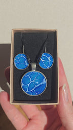 Rundes Cabochon-Schmuckset mit Anhänger und Ohrringen an schwarzem Band, in leuchtendem Blau und Cyan mit feinen weissen, verzweigten Linien.