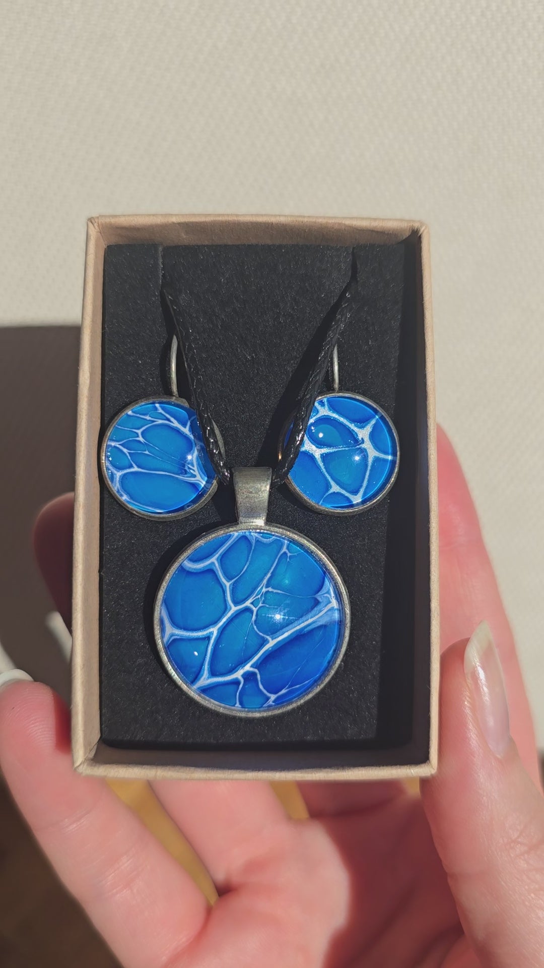 Rundes Cabochon-Schmuckset mit Anhänger und Ohrringen an schwarzem Band, in leuchtendem Blau und Cyan mit feinen weissen, verzweigten Linien.