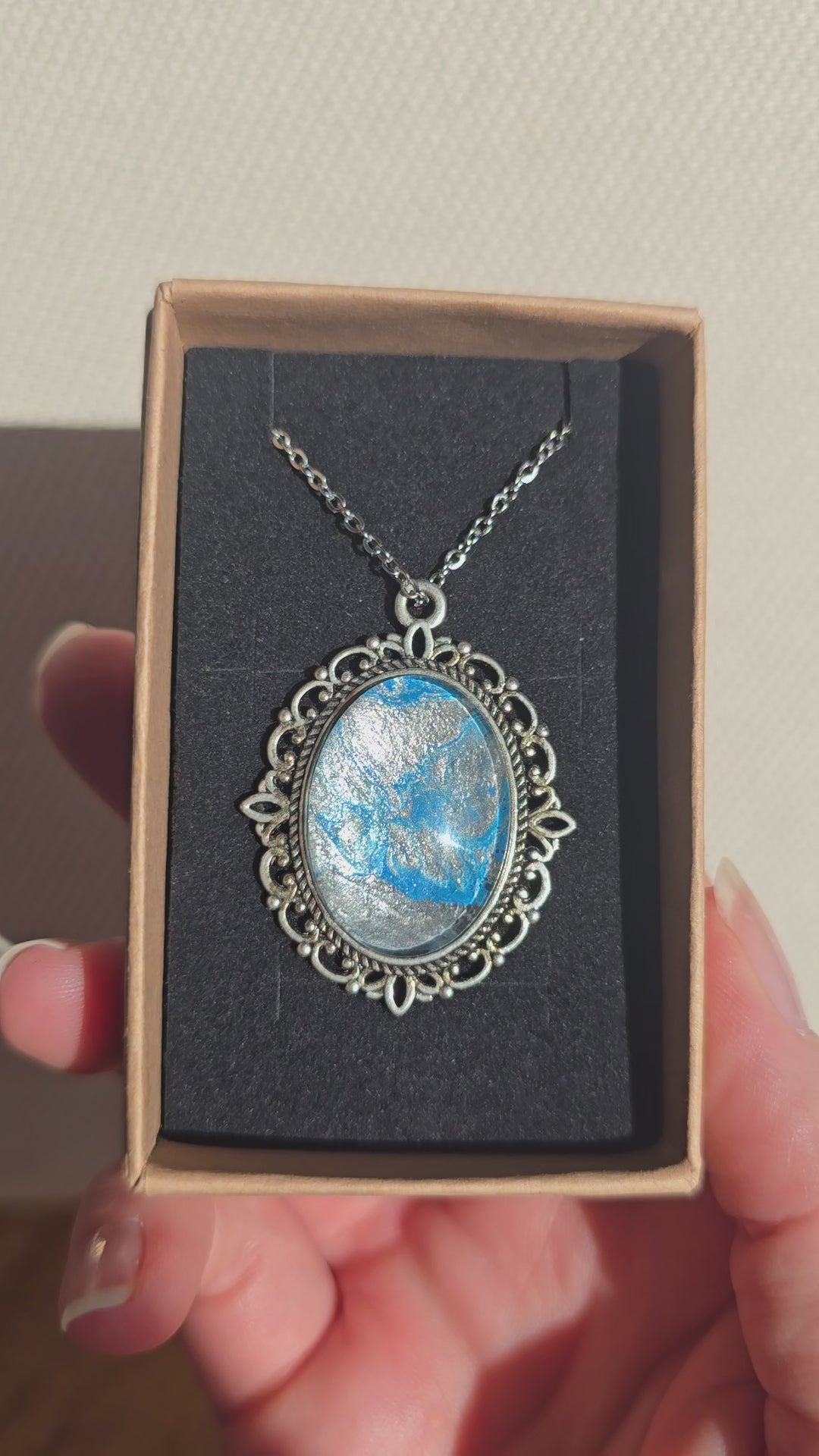 Ovale Cabochon Kette Solas Frozen Current in leuchtendem Blau, Silber und Grau mit verzierter silberfarbener Fassung und Metallkette.
