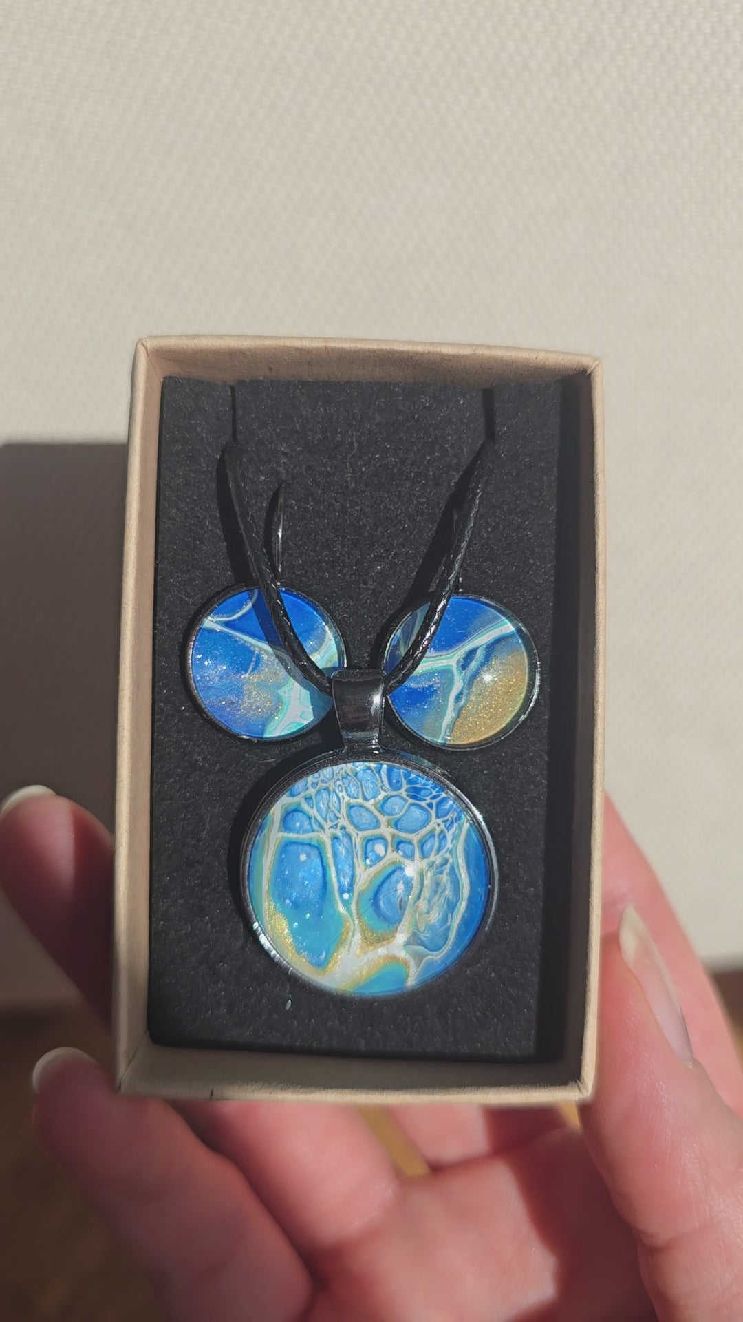 Rundes Cabochon Schmuckset mit schwarzer Kette und zwei Ohrringen, abstrakte Muster in Blau, Türkis, Weiss und Gold mit feinen netzartigen Strukturen.
