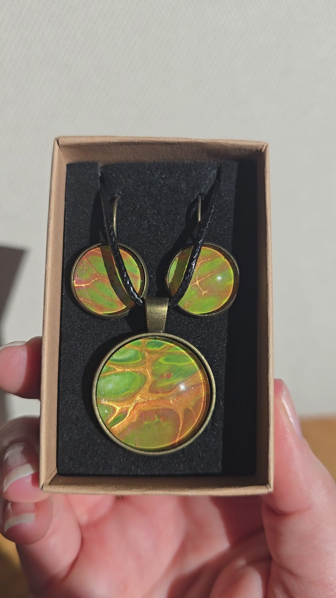 Rundes Cabochon Schmuckset mit grossem Kettenanhänger und zwei passenden Ohrringen in Grün, Orange und Gold mit fliessenden, organischen Mustern, bronzefarbenen Fassungen und schwarzem Band.
