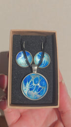 Rundes Cabochon-Schmuckset mit grossem Halskettenanhänger und zwei passenden Ohrringen in leuchtendem Blau auf silbrig-türkisem Grund.