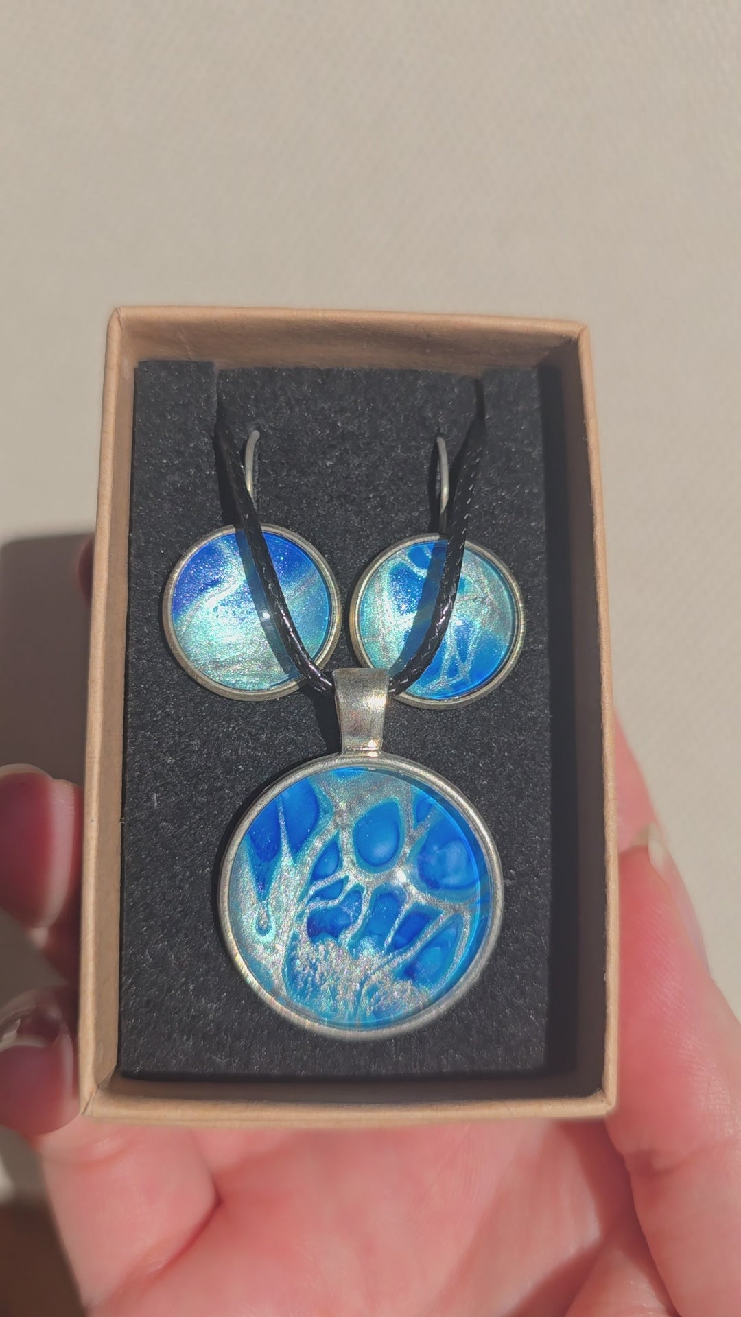 Rundes Cabochon-Schmuckset mit grossem Halskettenanhänger und zwei passenden Ohrringen in leuchtendem Blau auf silbrig-türkisem Grund.