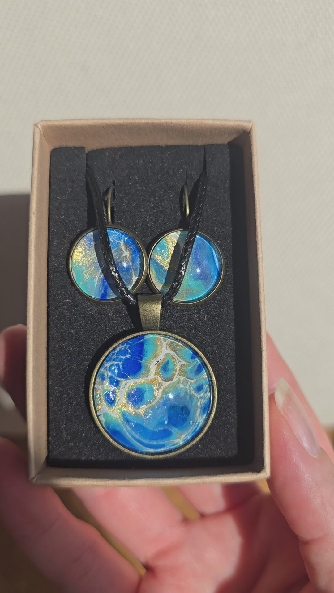 Rundes Cabochon-Schmuckset mit Anhänger und Ohrringen an schwarzem Band, mit organischem Muster in Blau, Türkis und Aquatönen sowie goldenen Akzenten.