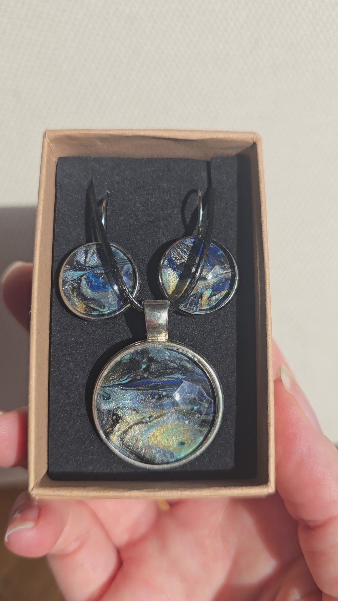 Rundes Cabochon-Schmuckset mit Anhänger und Ohrringen an schwarzem Band, mit fliessendem Muster in Dunkelblau, Schwarz und Petrol sowie goldenen Akzenten.