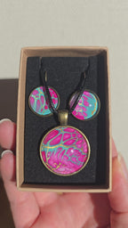 Cabochon-Schmuckset mit rundem Anhänger und zwei Ohrringen in kräftigem Pink und Türkis mit feinen goldenen Zellstrukturen und schwarzem Textilband.