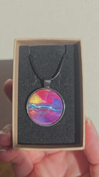 Runder Cabochon-Anhänger an schwarzem Band mit geschichtetem Muster in Fuchsia, Pink, Violett, Blau, Türkis und einem goldenen Akzent.