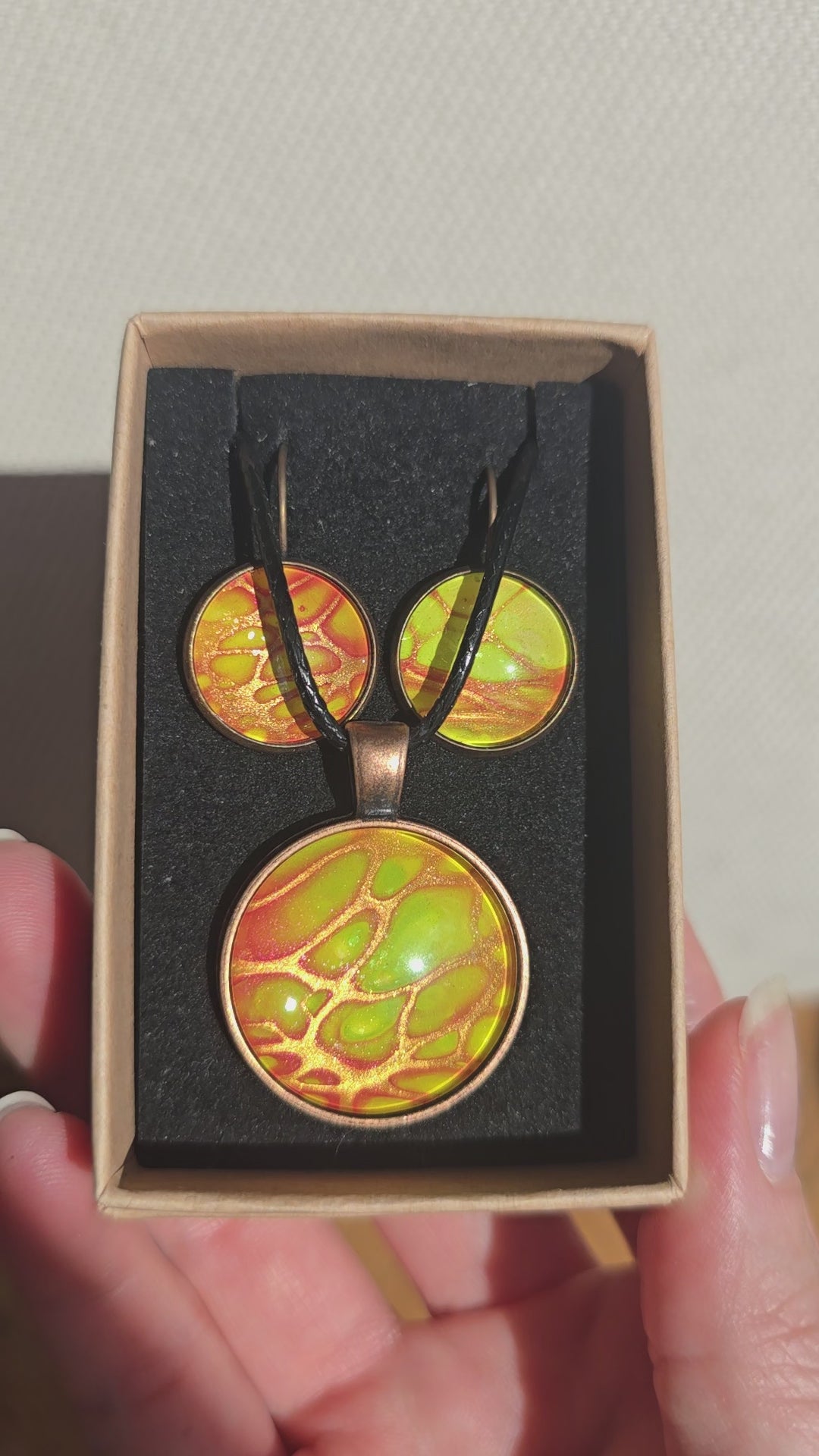 Rundes Cabochon-Schmuckset mit Anhänger und Ohrringen an schwarzem Band, mit organischem Muster in Gelb, Limettengrün und Orange, durchzogen von goldenen Adern.