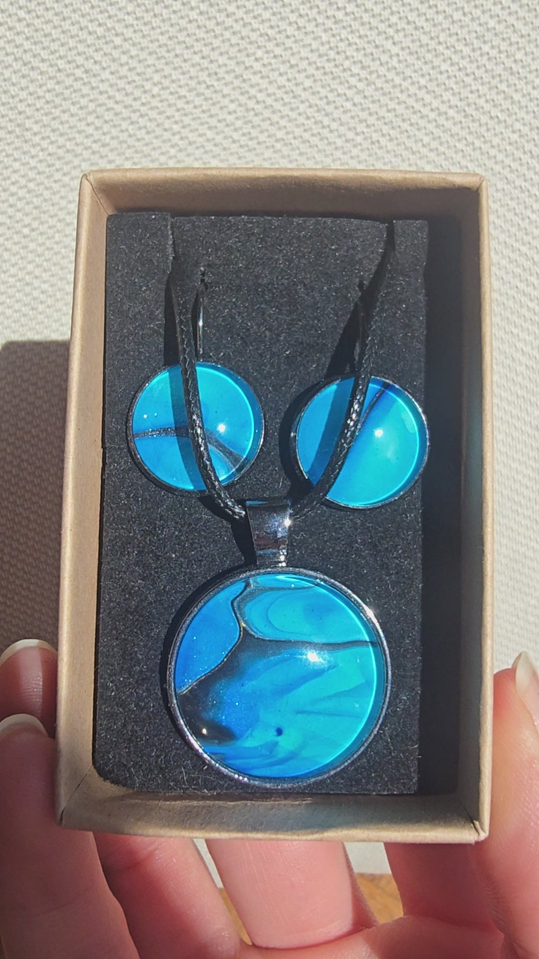 Handgefertigtes Schmuckset Solas Laguna mit rundem Anhänger und passenden Ohrringen in Blau- und Türkistönen mit fliessendem Marmormuster unter Glas.