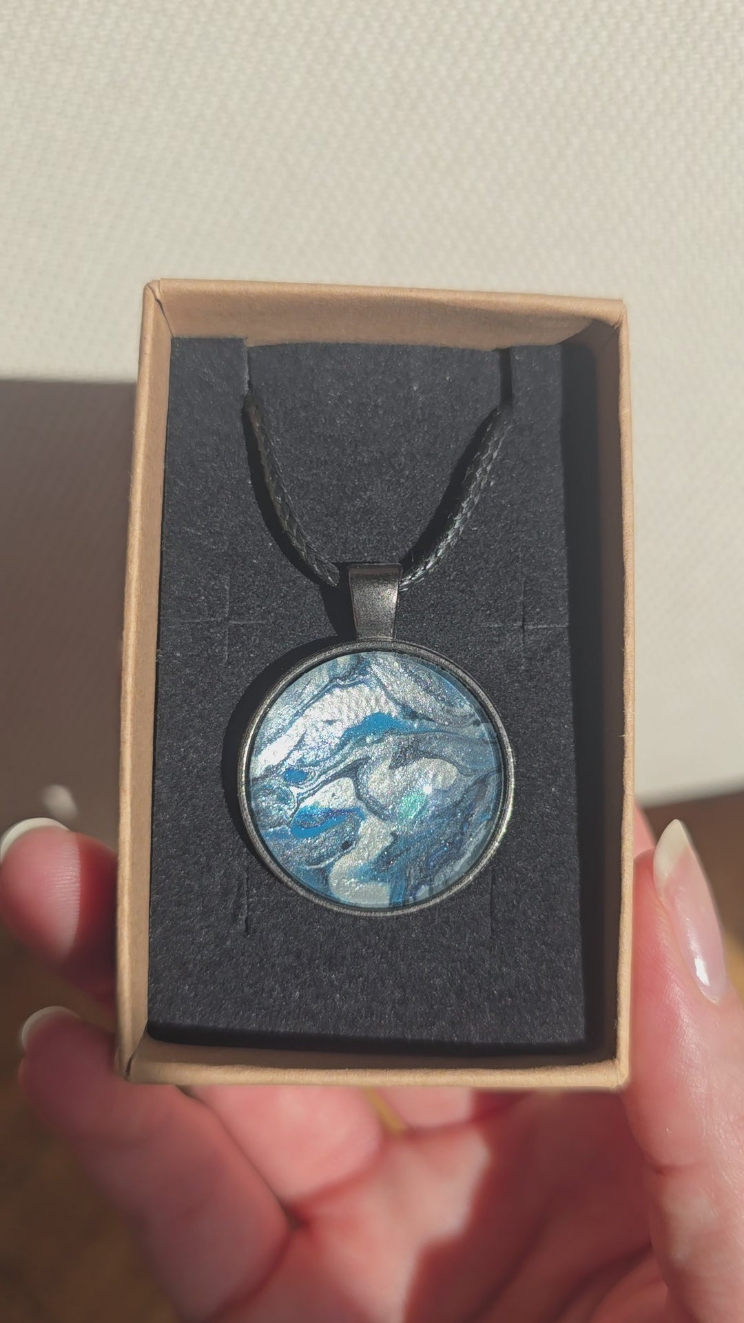 Runde Cabochon-Kette mit fliessendem Muster in Silber, Anthrazit, Eisblau und Türkis in dunkler Metallfassung.