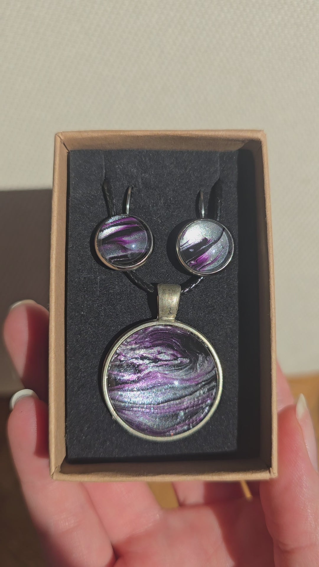 Rundes Cabochon-Schmuckset mit Anhänger und Ohrringen an schwarzem Band, mit fliessendem Muster in Violett, Pflaume, Silber und Schwarz.