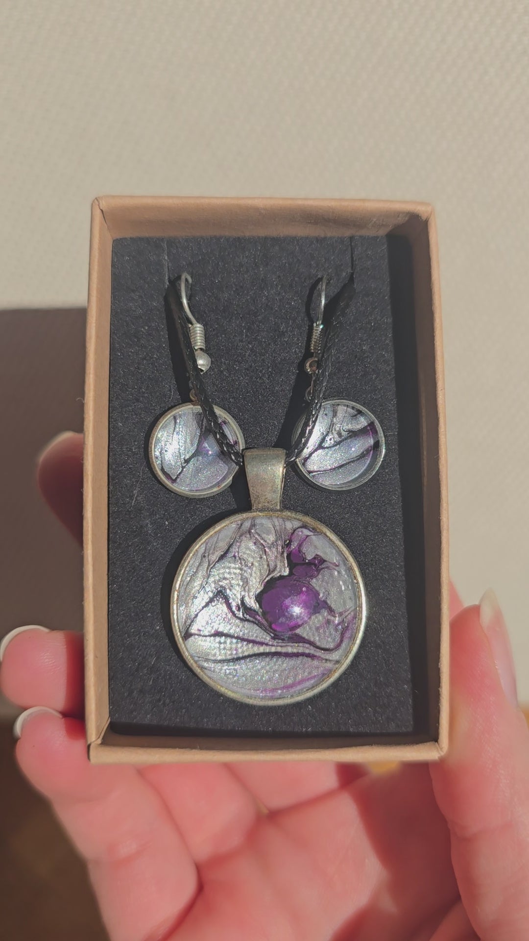 Cabochon-Schmuckset mit rundem Anhänger und zwei Ohrringen in schimmerndem Silber und Grau mit dunklen marmorierten Adern und violettem Farbkern.
