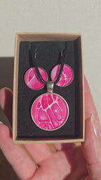 Rundes Cabochon-Schmuckset mit Anhänger und Ohrringen an schwarzem Band, mit organischem Muster in Fuchsia, Himbeerrosa und Pink sowie feinen hellen Linien.