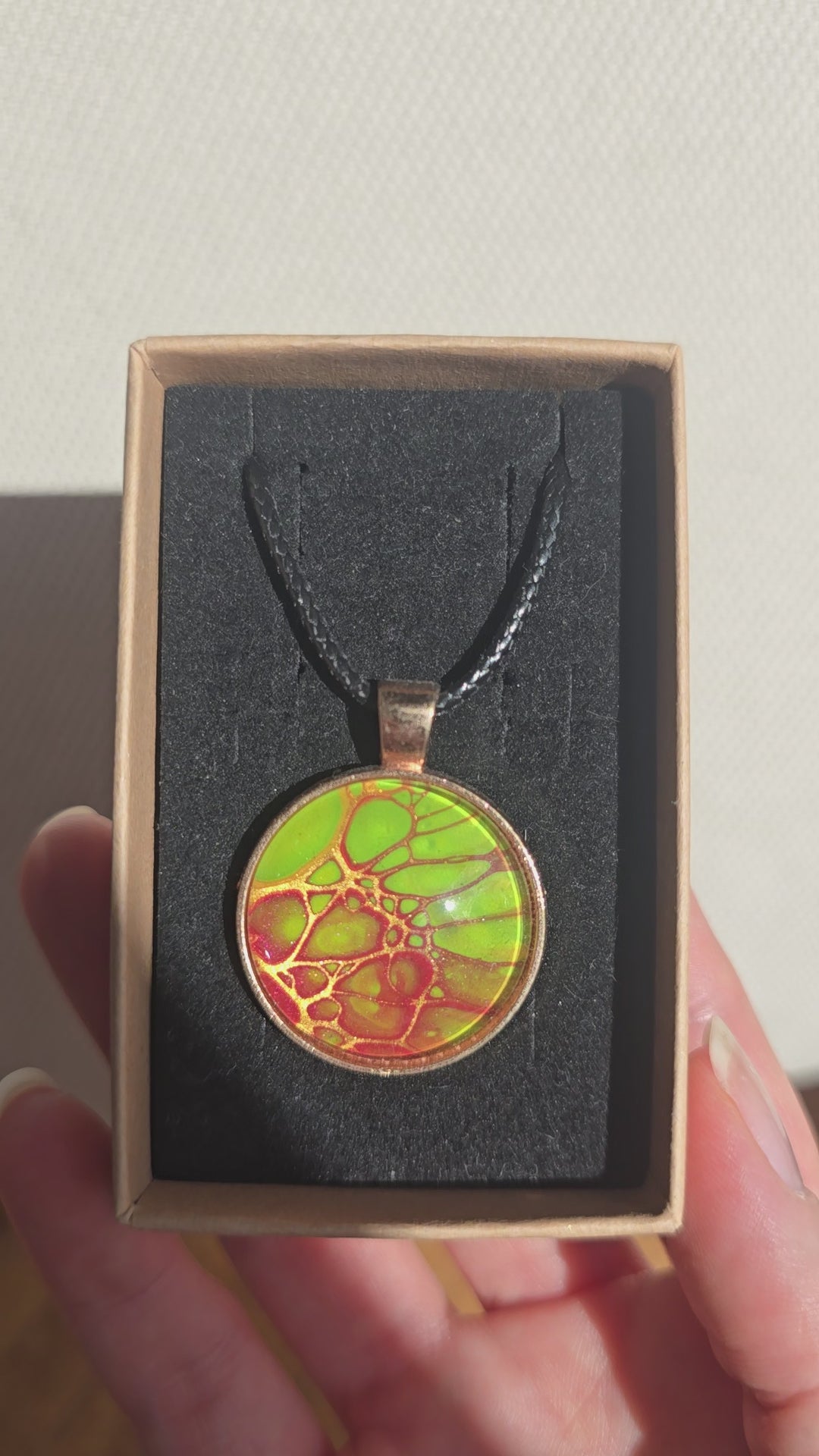 Runde Cabochon Kette Solas Bloom Temper mit leuchtend grüner, kupferroter Farbstruktur, bronzefarbener Fassung und schwarzem Band.