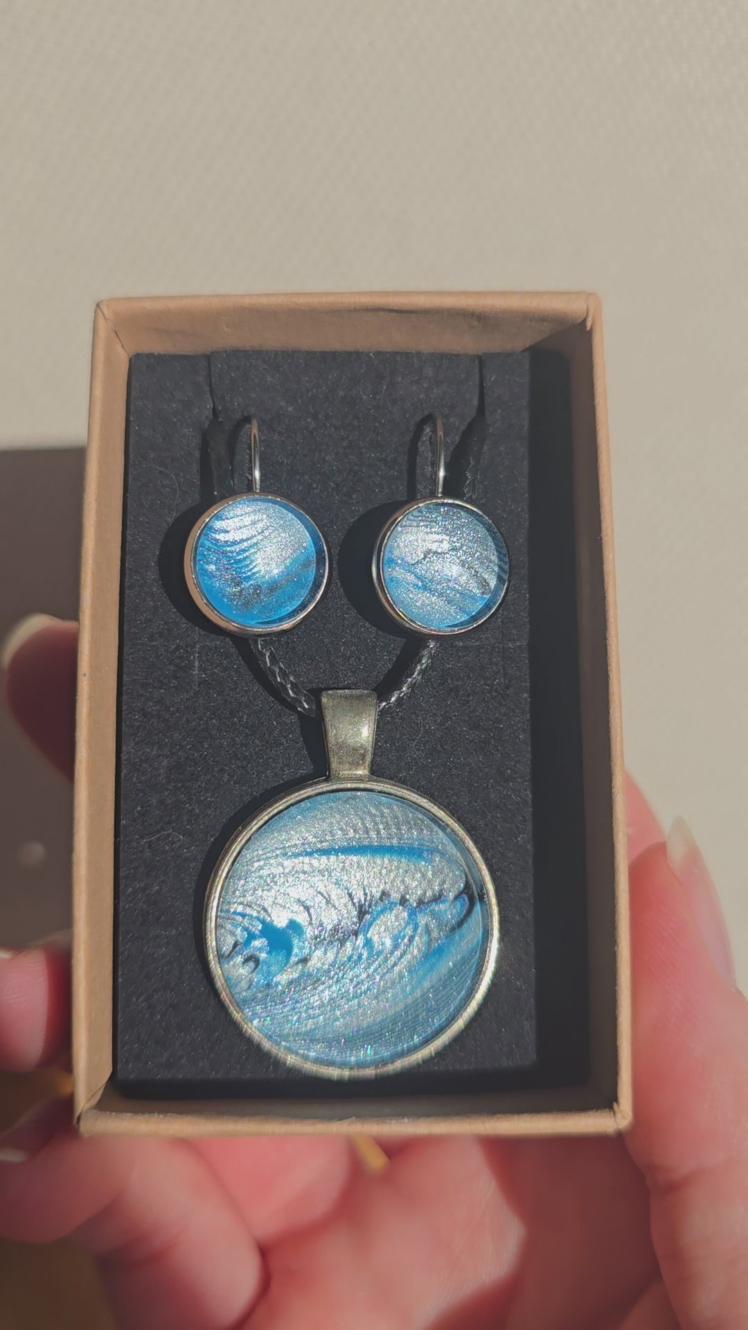 Rundes Cabochon-Schmuckset mit Anhänger und Ohrringen an schwarzem Band, mit fliessendem abstraktem Muster in Cyan, Blau, Grau und Schwarz.