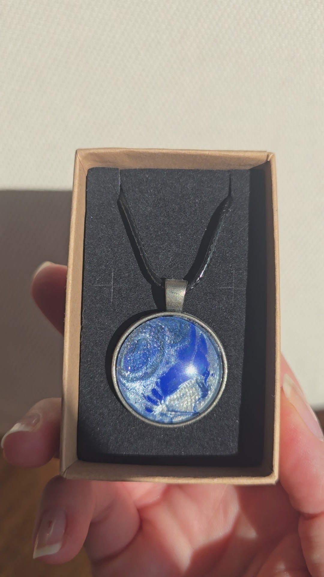 Runde Cabochon Kette Solas Blue Glacier in Kobaltblau, Silber und Weiss mit dunkler Metallfassung und schwarzem Band.