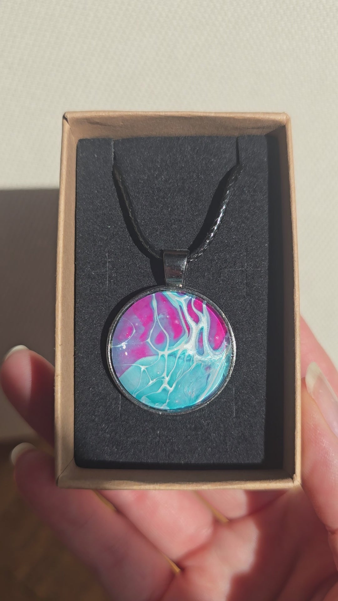 Runder Cabochon-Anhänger an schwarzem Band mit verzweigtem, organischem Muster in Türkis, Aqua, Fuchsia, Pink und hellen Linien.
