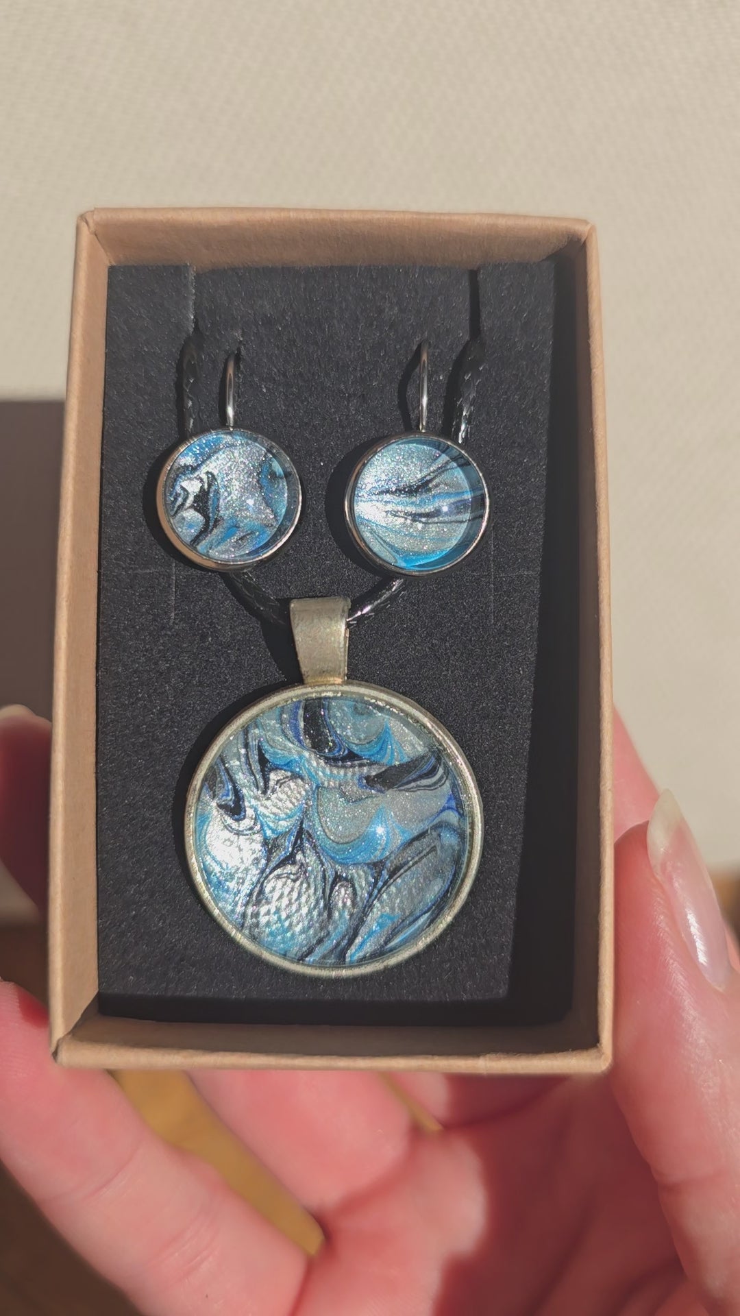 Rundes Cabochon-Schmuckset mit Anhänger und Ohrringen an schwarzem Band, mit marmoriertem Muster in Blau, Cyan, Silber-/Perlgrau, Anthrazit und Schwarz.