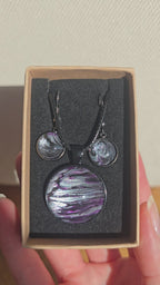 Rundes Cabochon-Schmuckset mit Anhänger und Ohrringen an schwarzem Band, mit geschichtetem Muster in Schwarz, Anthrazit, Violett und silbrigem Schimmer.