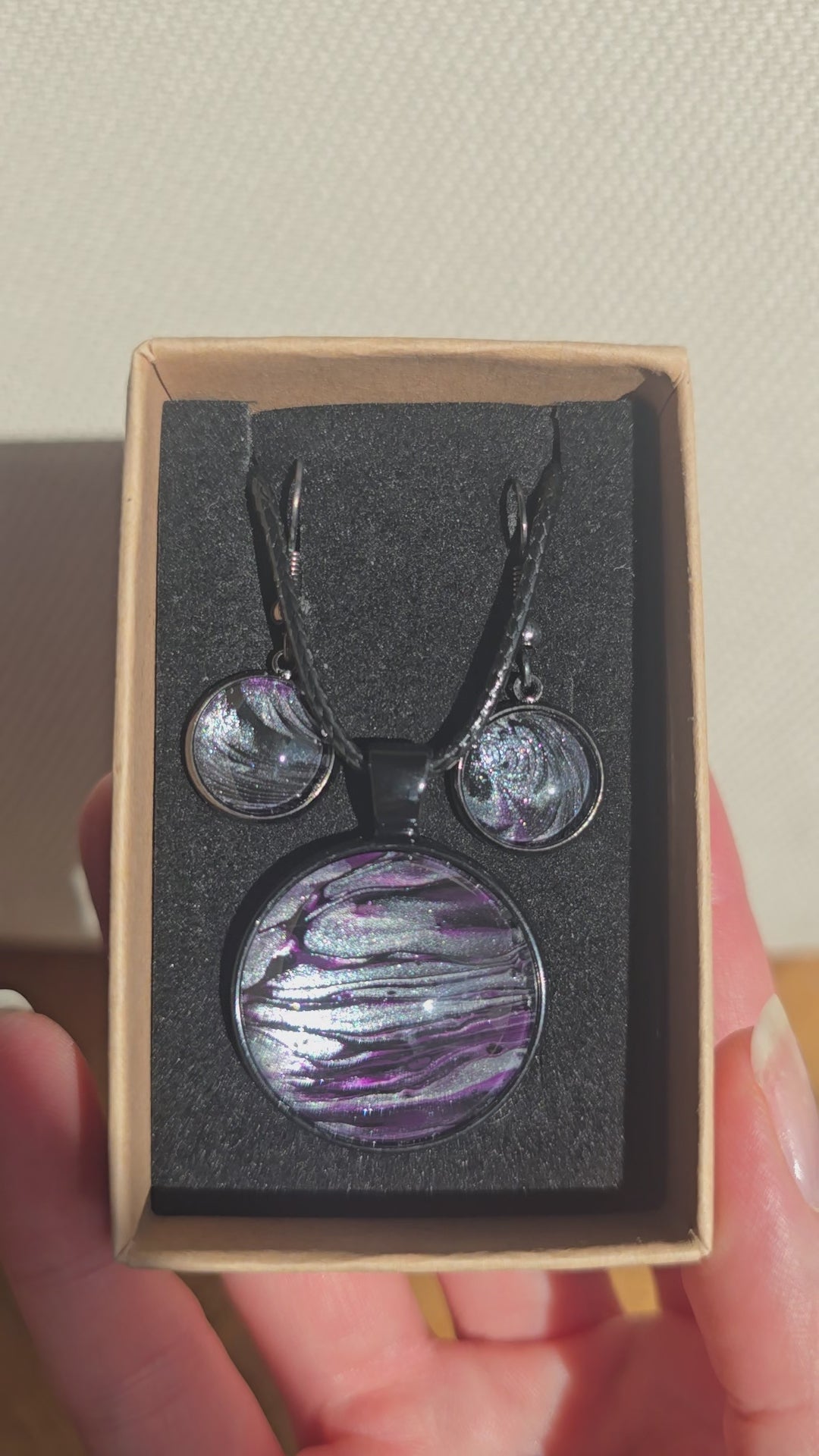 Rundes Cabochon-Schmuckset mit Anhänger und Ohrringen an schwarzem Band, mit geschichtetem Muster in Schwarz, Anthrazit, Violett und silbrigem Schimmer.