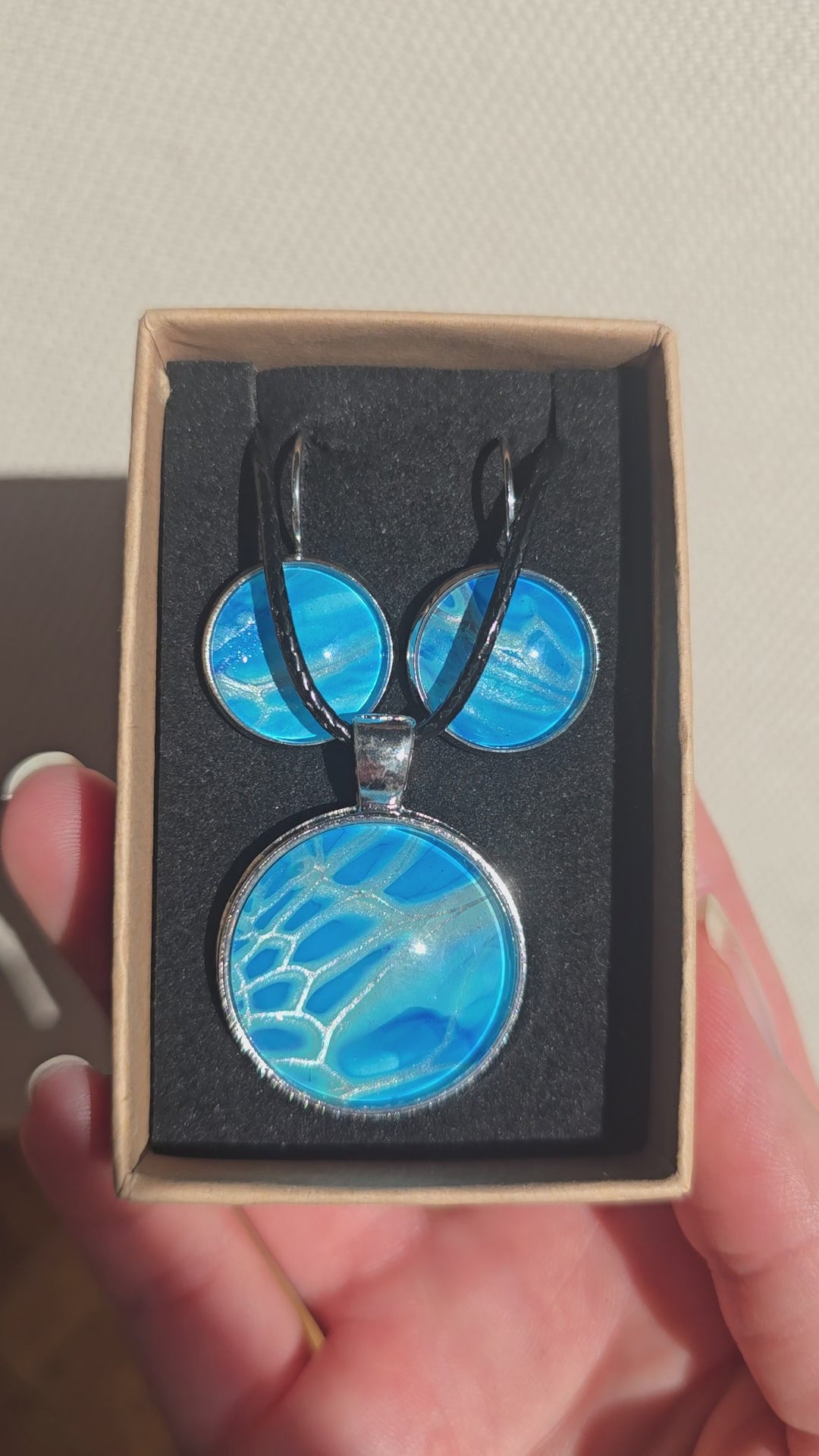 Rundes Cabochon-Schmuckset mit Anhänger und Ohrringen an schwarzem Band, mit organischem Muster in Türkis, Cyan und Blau sowie silbernem Schimmer.
