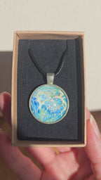 Runder Cabochon-Anhänger an schwarzem Band mit filigranem, netzartigem Muster in Aqua-, Türkis-, Hellblau- und Cremetönen.