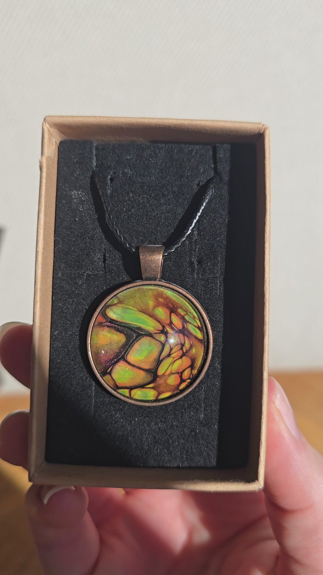 Runde Cabochon Kette Solas Forest Flame in Grün, Orange und Gold mit dunklen Strukturen, bronzefarbener Fassung und schwarzem Band.