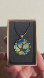 Runder Cabochon-Anhänger an schwarzem Band mit organischem Muster in Türkis, tiefem Blau, Schwarz und warm schimmernden Goldtönen.