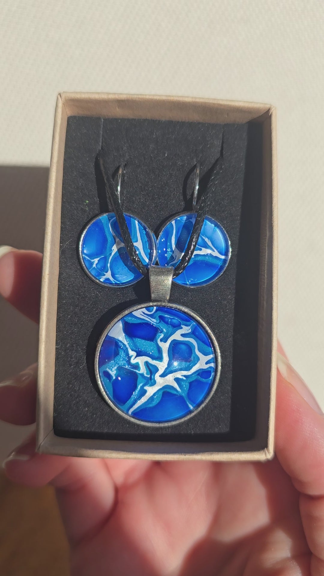Rundes Cabochon Schmuckset mit grossem Kettenanhänger und zwei passenden Ohrringen in kräftigem Blau und Türkis mit weissen, verzweigten Strukturen, silberfarbenen Fassungen und schwarzem Band.
