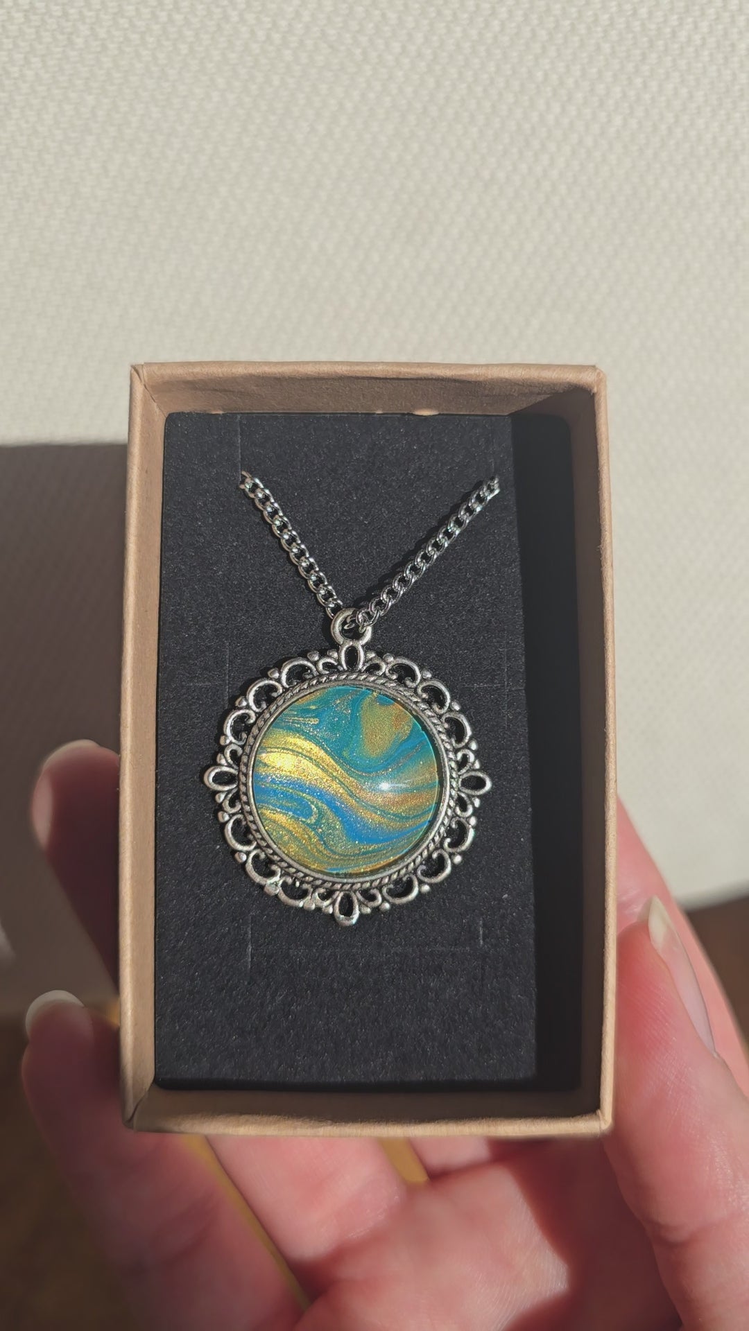 Runde Cabochon Kette Solas Sunlit Current in Türkis, Blau und Gold mit verzierter silberfarbener Fassung und Metallkette.