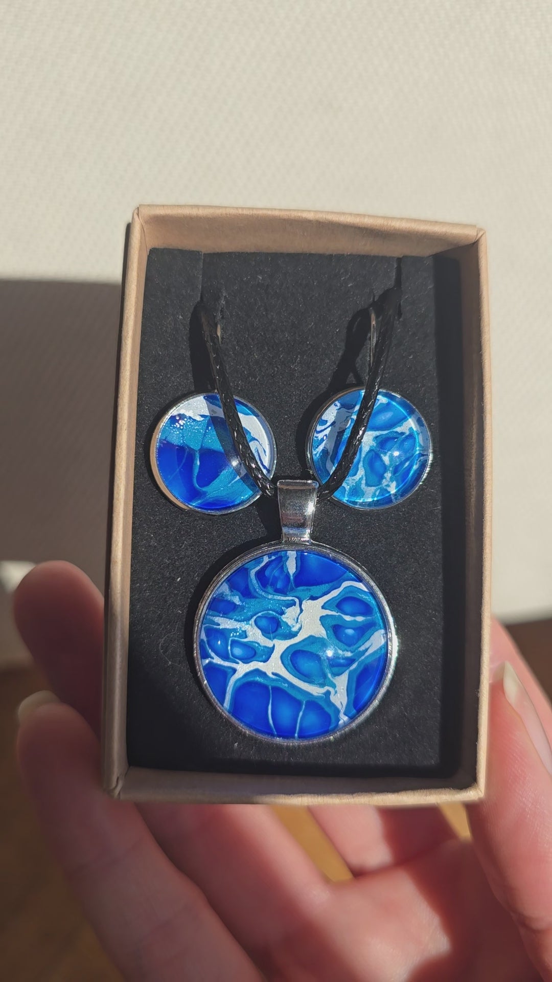 Cabochon Schmuckset Solas Blue Fusion mit runder Kette und zwei Ohrringen in Dunkelblau, Kobaltblau, Türkis und Weiss, silberfarbenen Fassungen und schwarzem Band.
