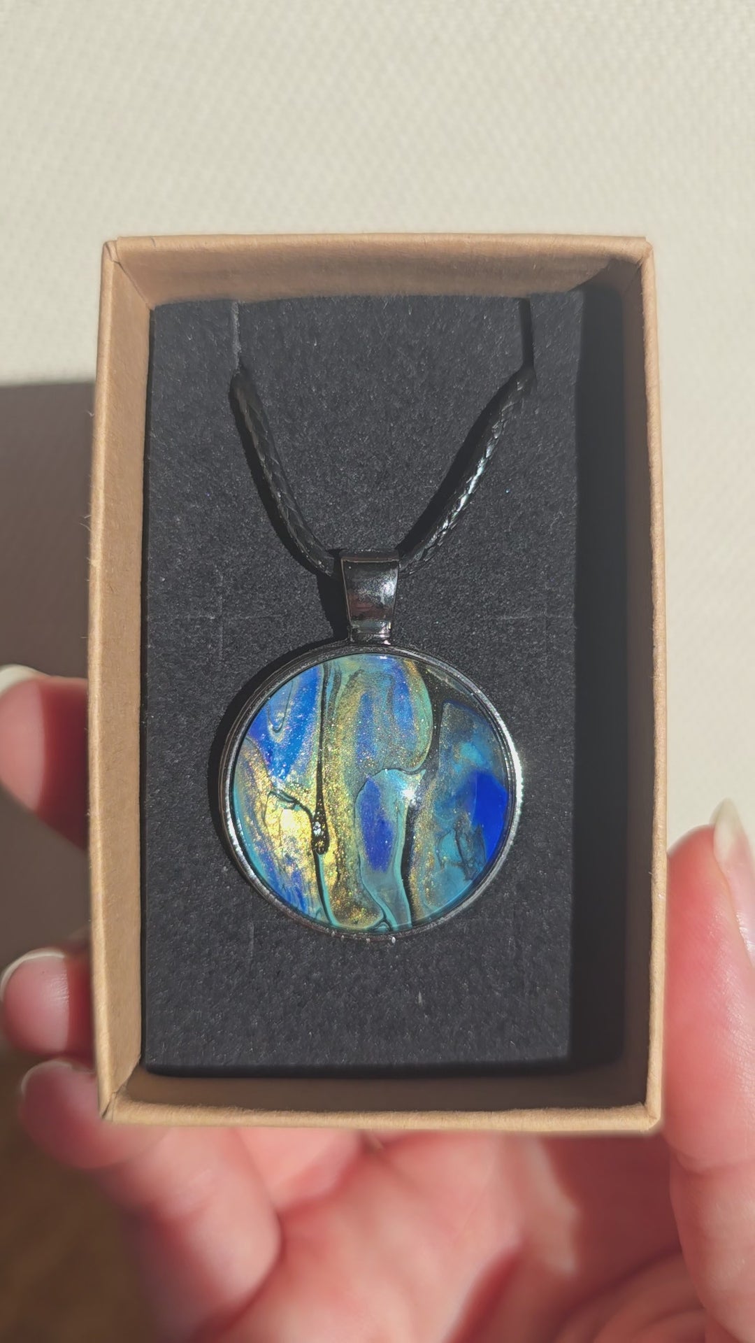 Runde Cabochon Kette Solas Ocean Veil in Blau, Türkis, Petrol und Grün mit dunkler Metallfassung und schwarzem Band.
