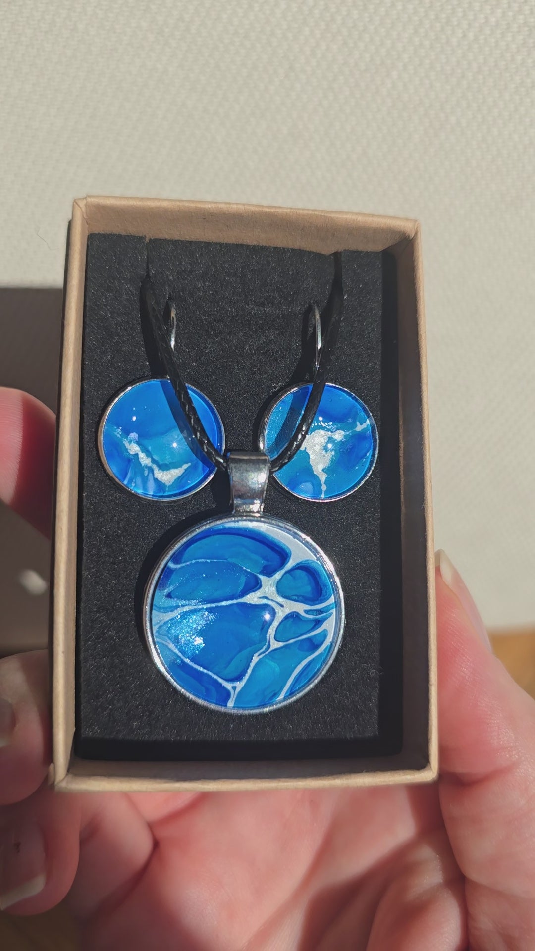 Rundes Cabochon-Schmuckset mit Anhänger und Ohrringen an schwarzem Band, mit organischem Inselmuster in Kobaltblau, Azurblau, Cyan und hellen Linien.