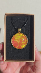 Runde Cabochon Kette Solas Golden Heat mit abstraktem Muster in Orange, Gelb und Gold, goldfarbener Fassung und schwarzem Band.
