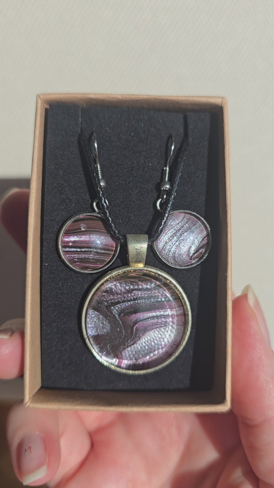 Rundes Cabochon-Schmuckset mit Anhänger und Ohrringen, abstrakt gemustert in Violett, Mauve, Schwarz und silbrig schimmernden Nuancen.