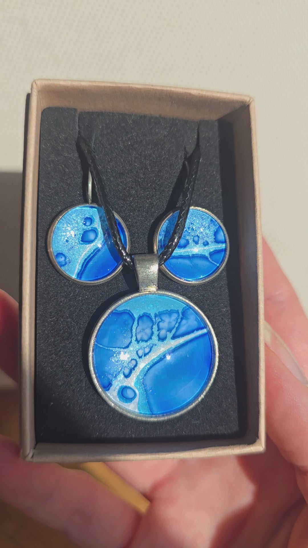 Rundes Cabochon-Schmuckset mit Anhänger und Ohrringen an schwarzem Band, in Kobaltblau, Cyan und Türkis mit runden Zellformen und dunkelblauen Konturen.