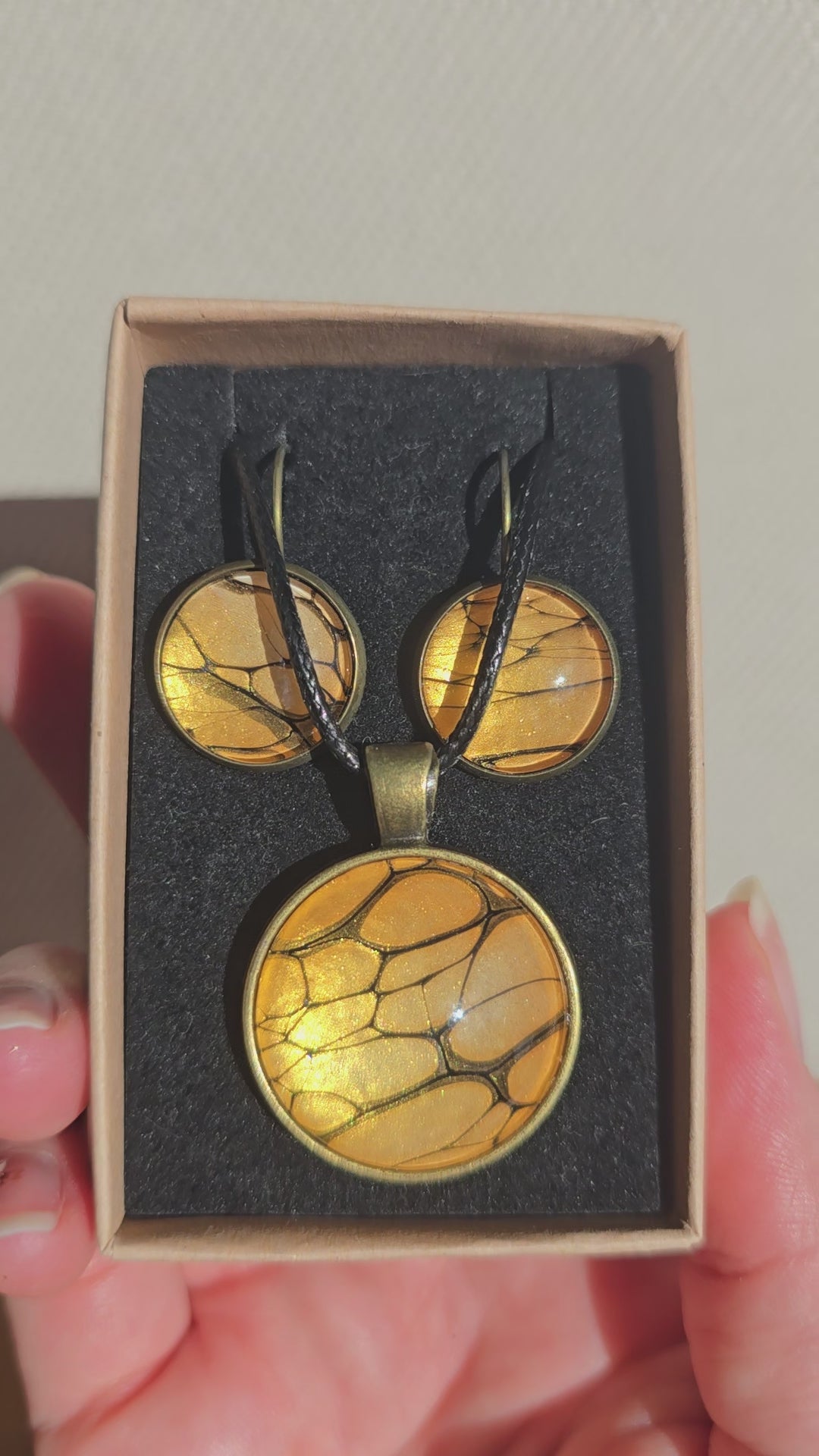 Rundes Cabochon-Schmuckset mit Halskettenanhänger und passenden Ohrringen in warmen Gold- und Bernsteintönen mit feinen dunklen Linien.