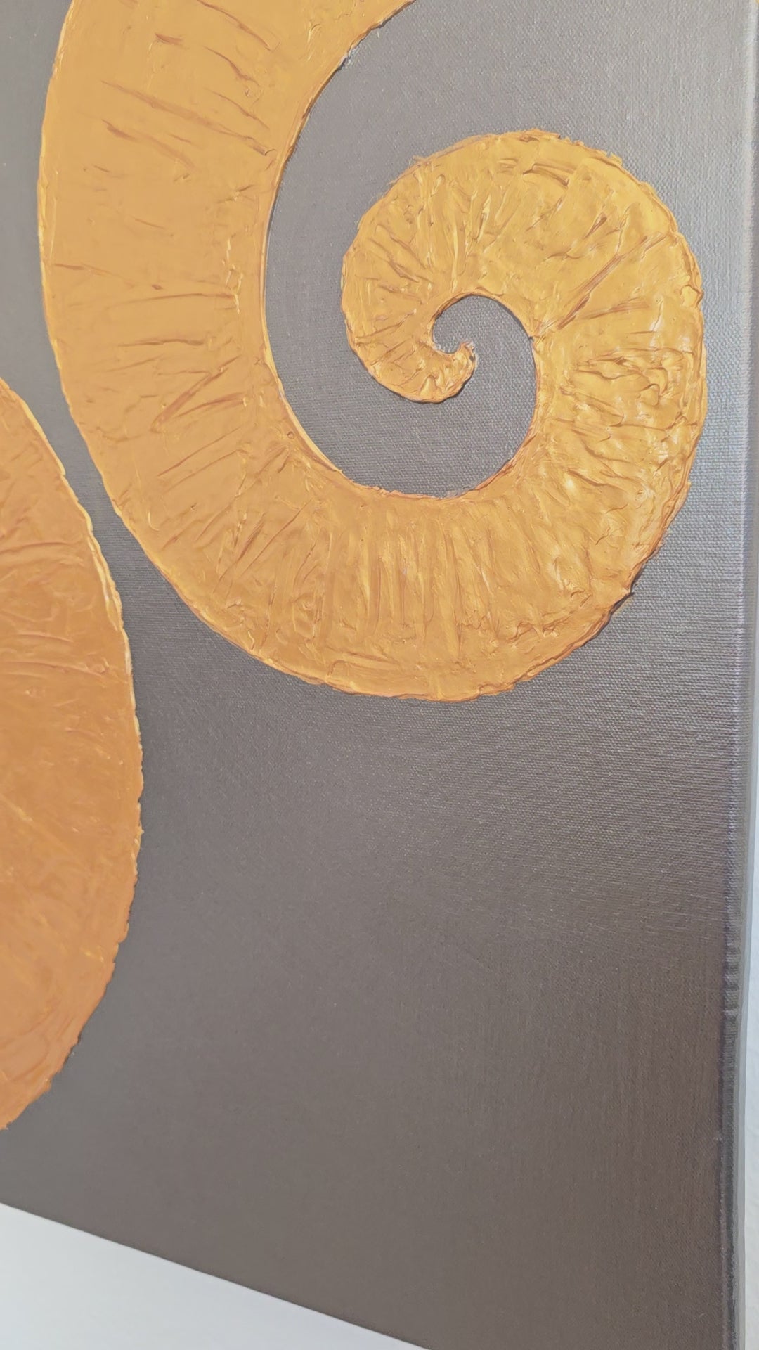 Quadratisches Leinwandbild mit warmgrauem Hintergrund und zwei grossen, plastisch strukturierten goldenen Spiralen.