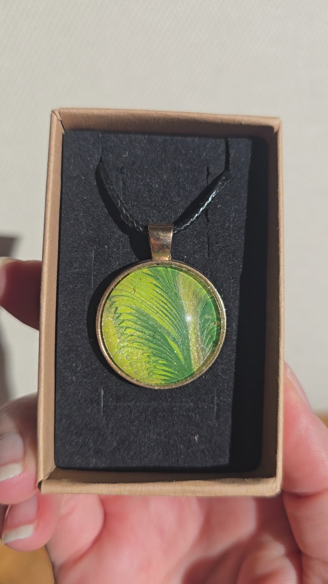 Runde Cabochon Kette Solas Wild Fern in verschiedenen Grün- und Goldtönen mit farnähnlicher Struktur, bronzefarbener Fassung und schwarzem Band.