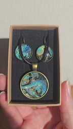 Cabochon-Schmuckset mit rundem Anhänger und zwei Ohrringen mit marmoriertem Muster in Türkis, Petrol, Blau und Schwarz mit goldig-bronzefarbenen Akzenten.