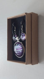 Cabochon-Schmuckset mit rundem Anhänger und zwei Ohrringen in dunklem Violett mit geschwungenen silbernen und irisierenden Perlmuttlinien sowie schwarzem Textilband.