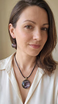 Frau trägt rundes Cabochon-Schmuckset mit Anhänger und Ohrringen, abstrakt gemustert in Violett, Mauve, Schwarz und silbrig schimmernden Nuancen.