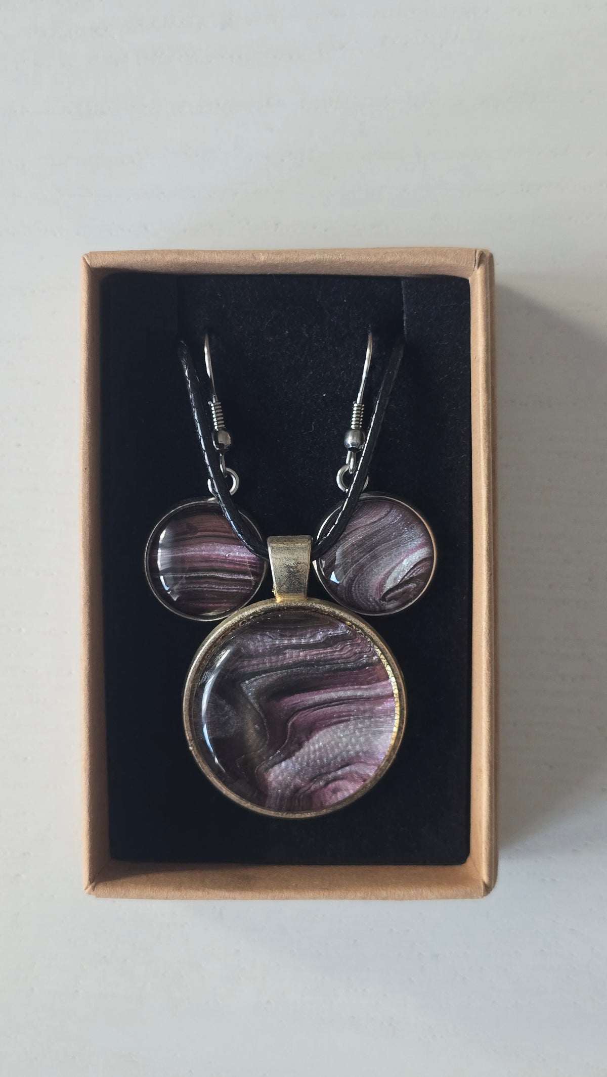 Rundes Cabochon-Schmuckset mit Anhänger und Ohrringen, abstrakt gemustert in Violett, Mauve, Schwarz und silbrig schimmernden Nuancen.