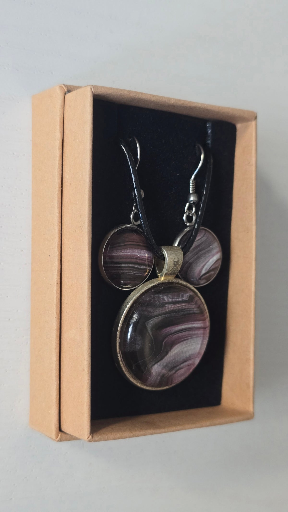 Rundes Cabochon-Schmuckset mit Anhänger und Ohrringen, abstrakt gemustert in Violett, Mauve, Schwarz und silbrig schimmernden Nuancen.