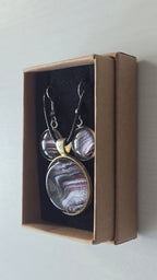 Rundes Cabochon-Schmuckset mit Anhänger und Ohrringen, abstrakt gemustert in Violett, Mauve, Schwarz und silbrig schimmernden Nuancen.