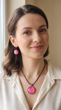 Frau trägt rundes Cabochon-Schmuckset mit Anhänger und Ohrringen an schwarzem Band, mit organischem Muster in Fuchsia, Himbeerrosa und Pink sowie feinen hellen Linien.